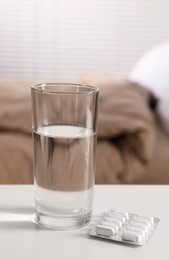 Photo of Glass of water and pills in blister on white table indoors