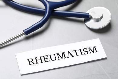 Photo of Sheet of paper with word Rheumatism and stethoscope on table, closeup