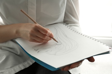 Photo of Woman drawing girl's portrait with pencil in notepad, closeup