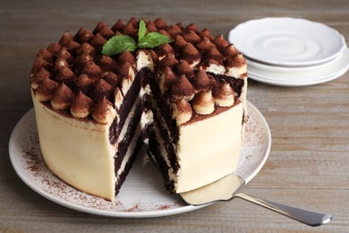 Photo of Delicious tiramisu cake with mint leaves and server on wooden table