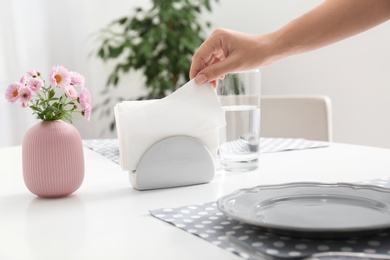Photo of Woman taking paper tissue from ceramic napkin holder on served table