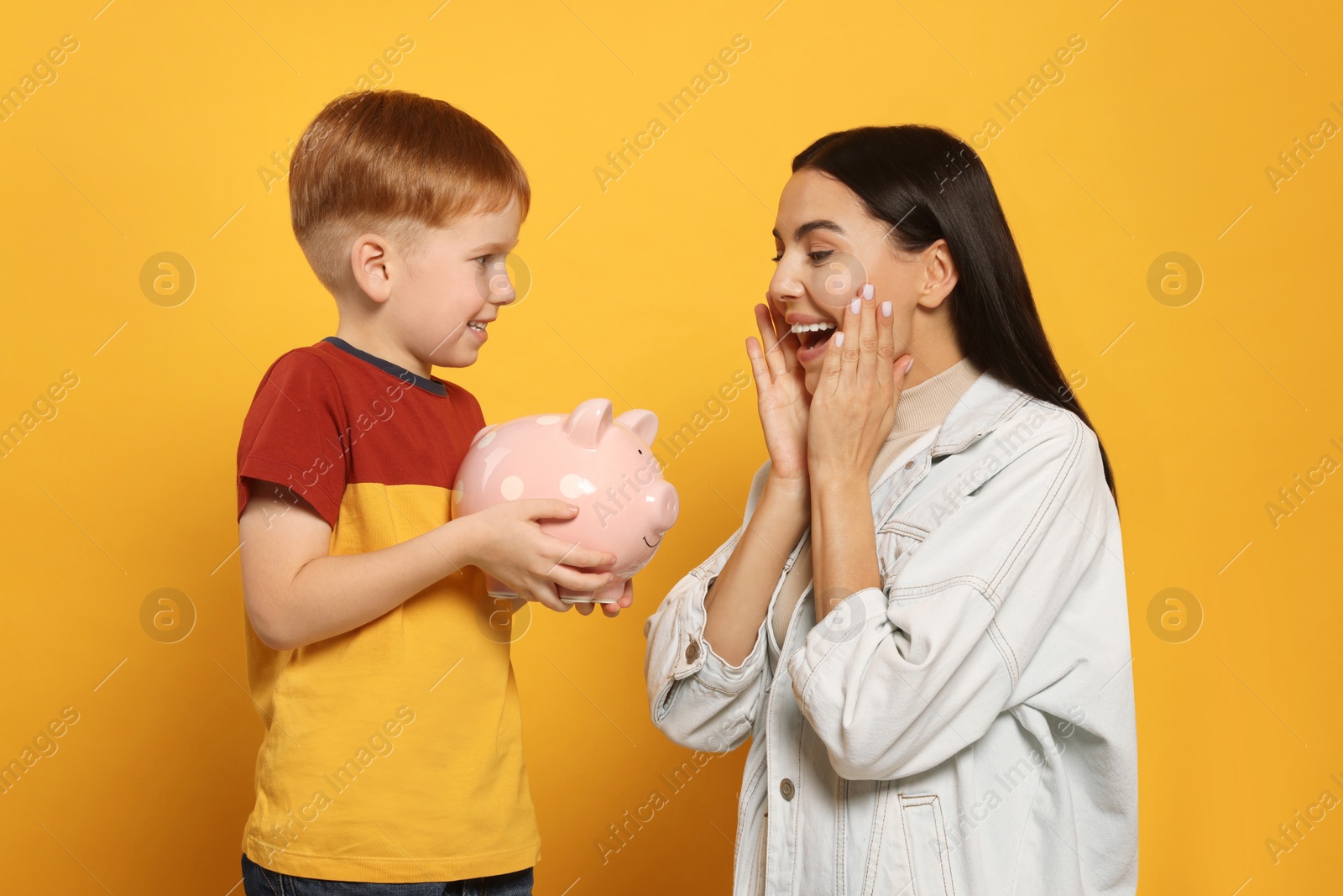 Photo of Mother and her son with ceramic piggy bank on orange background