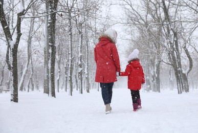 Photo of Mother with her child spending time outside on winter day, back view. Christmas vacation
