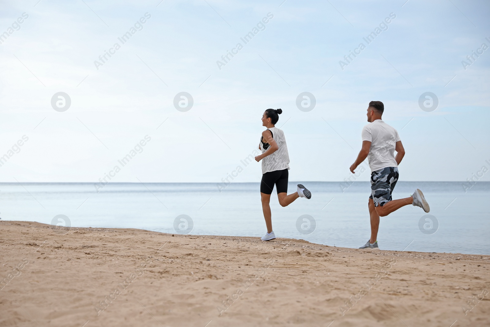 Photo of Couple running together on beach, space for text. Body training