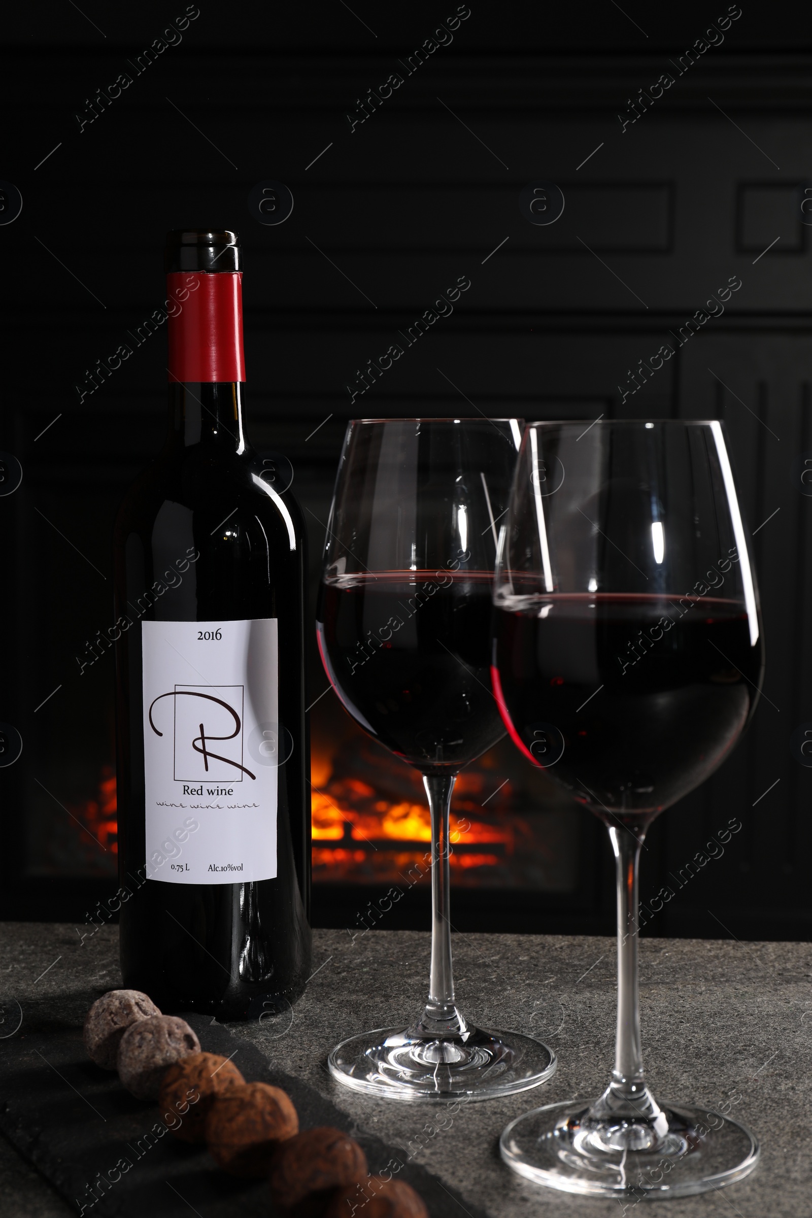 Photo of Red wine and chocolate truffles on gray table against fireplace