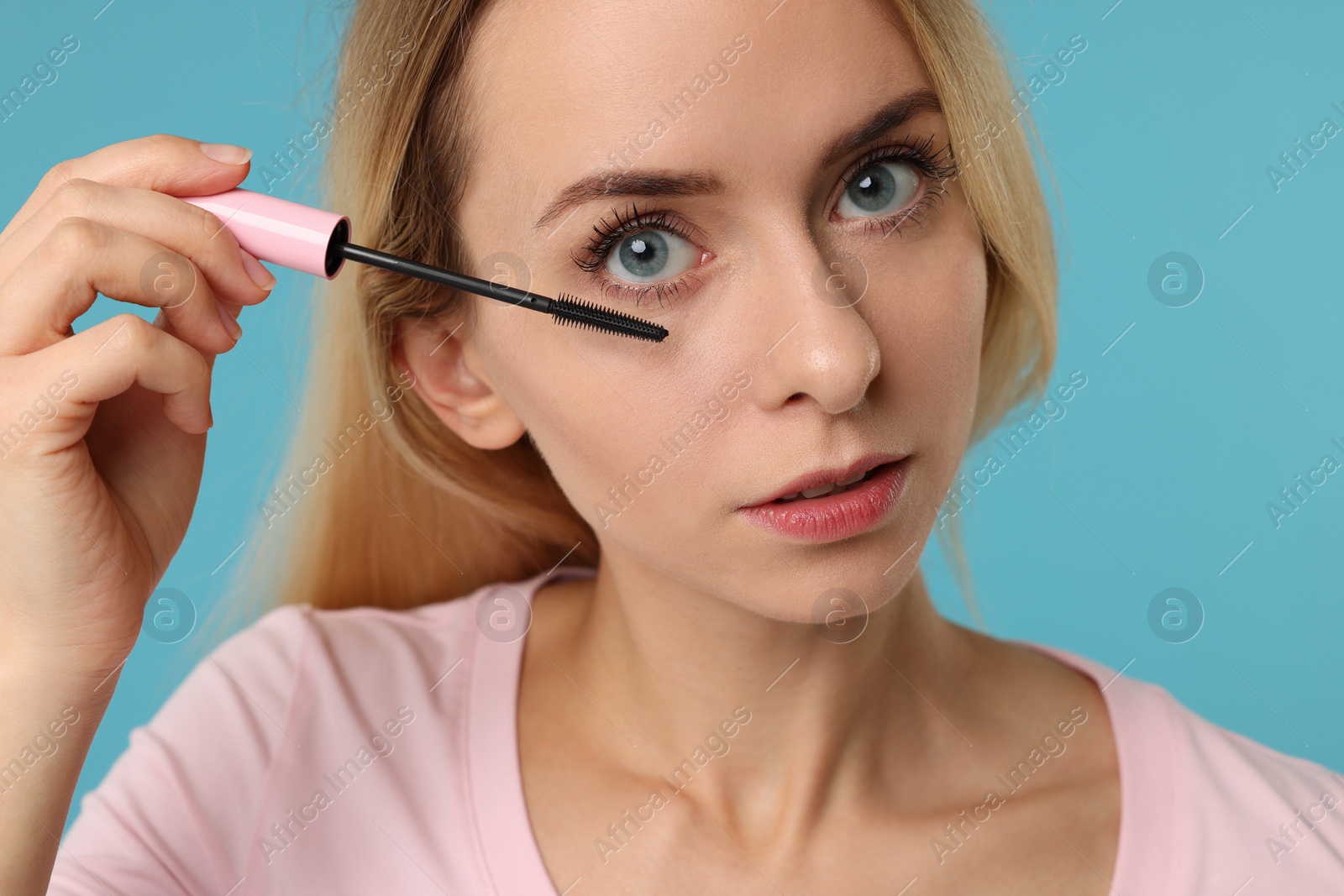 Photo of Beautiful woman applying mascara on light blue background, closeup