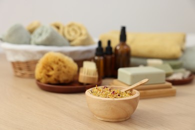 Photo of Bowl with dry flowers, soap bar and bottles of essential oils on light wooden table. Spa therapy