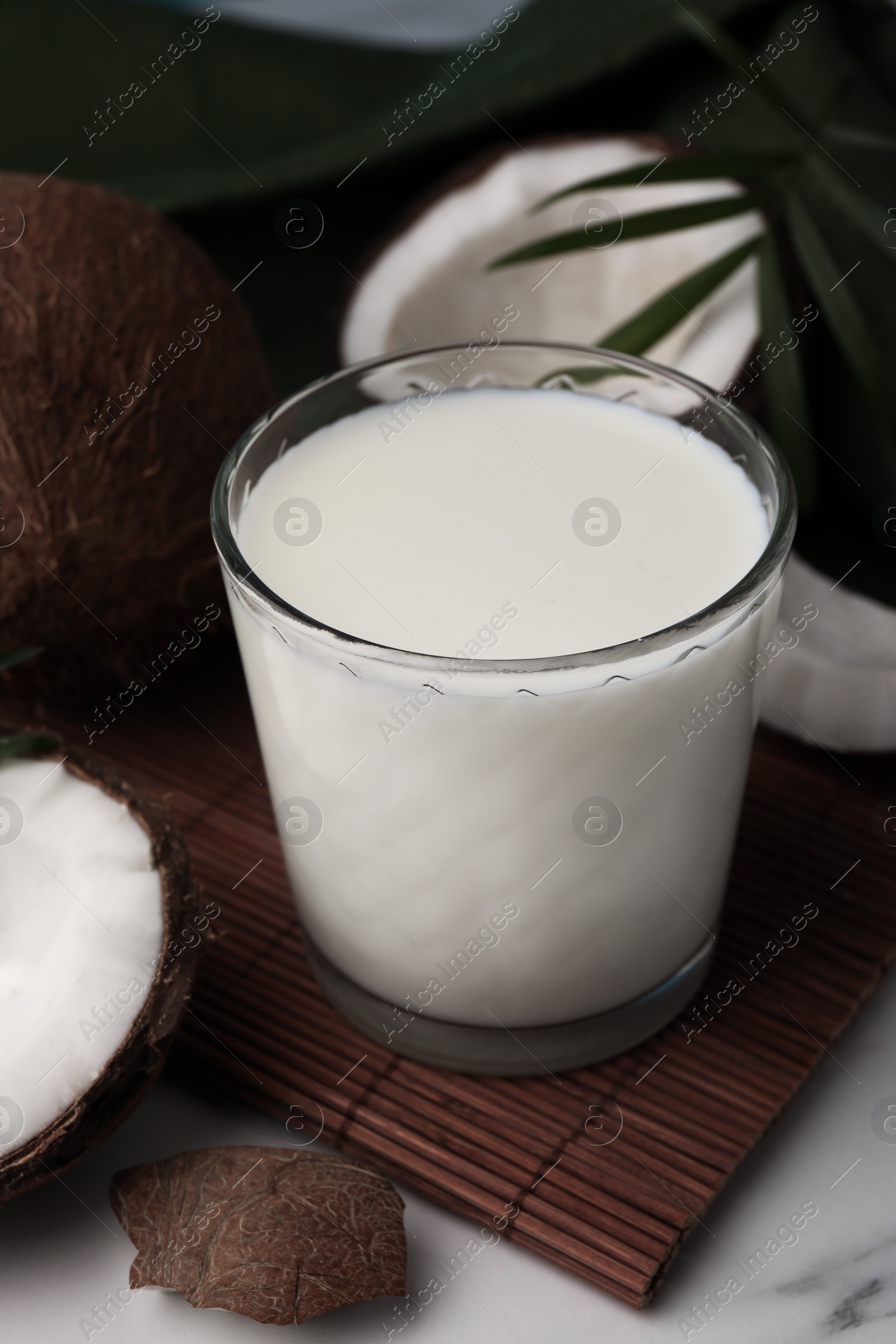 Photo of Glass of delicious vegan milk, coconut pieces and palm leaves on white marble table