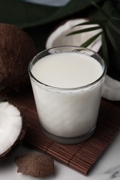 Glass of delicious vegan milk, coconut pieces and palm leaves on white marble table