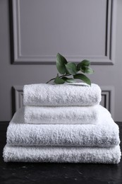 Stacked terry towels and green leaves on black textured table indoors