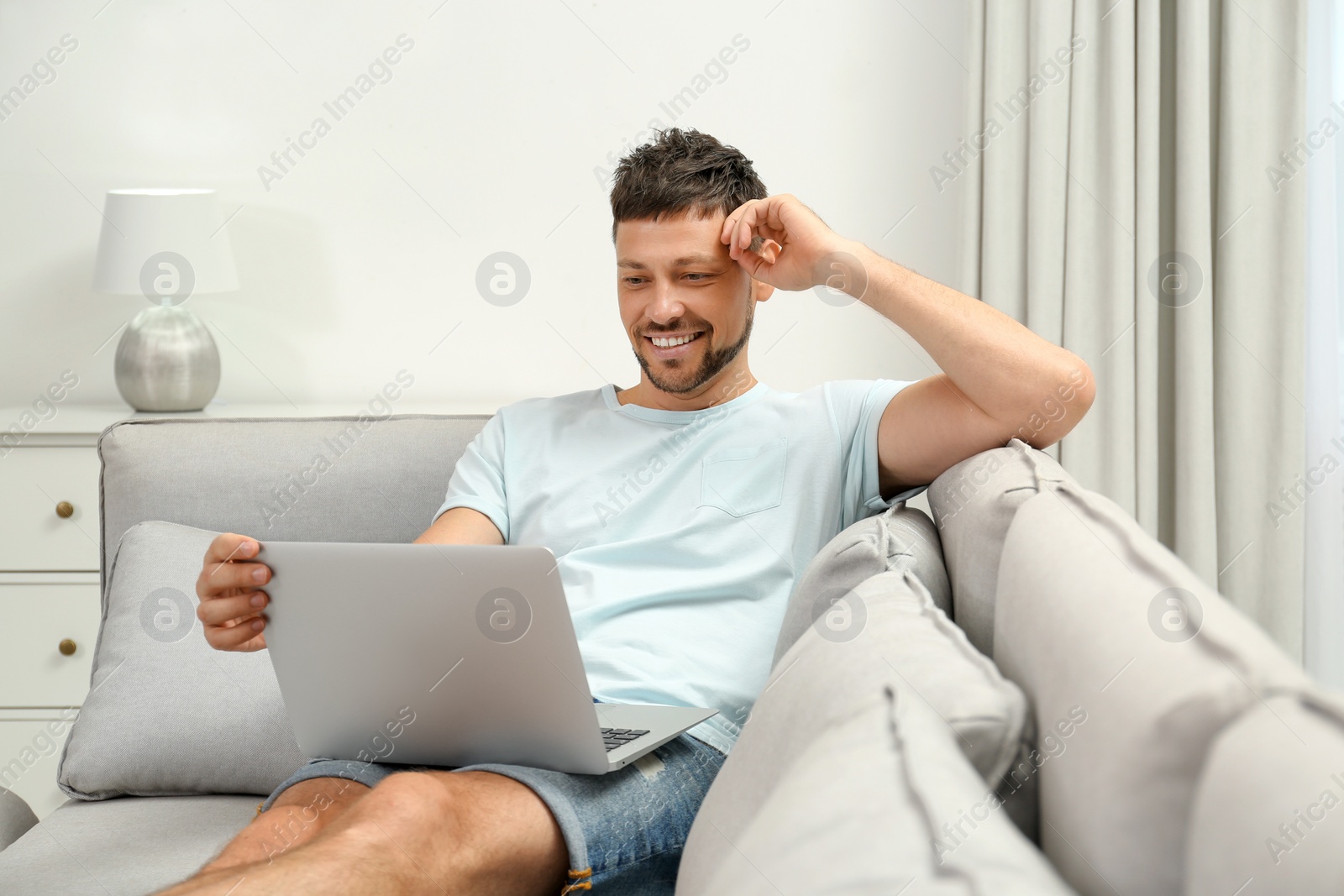 Photo of Happy man using laptop on sofa at home. Internet shopping