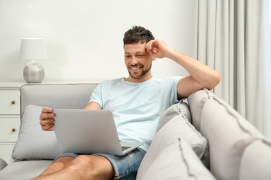 Happy man using laptop on sofa at home. Internet shopping