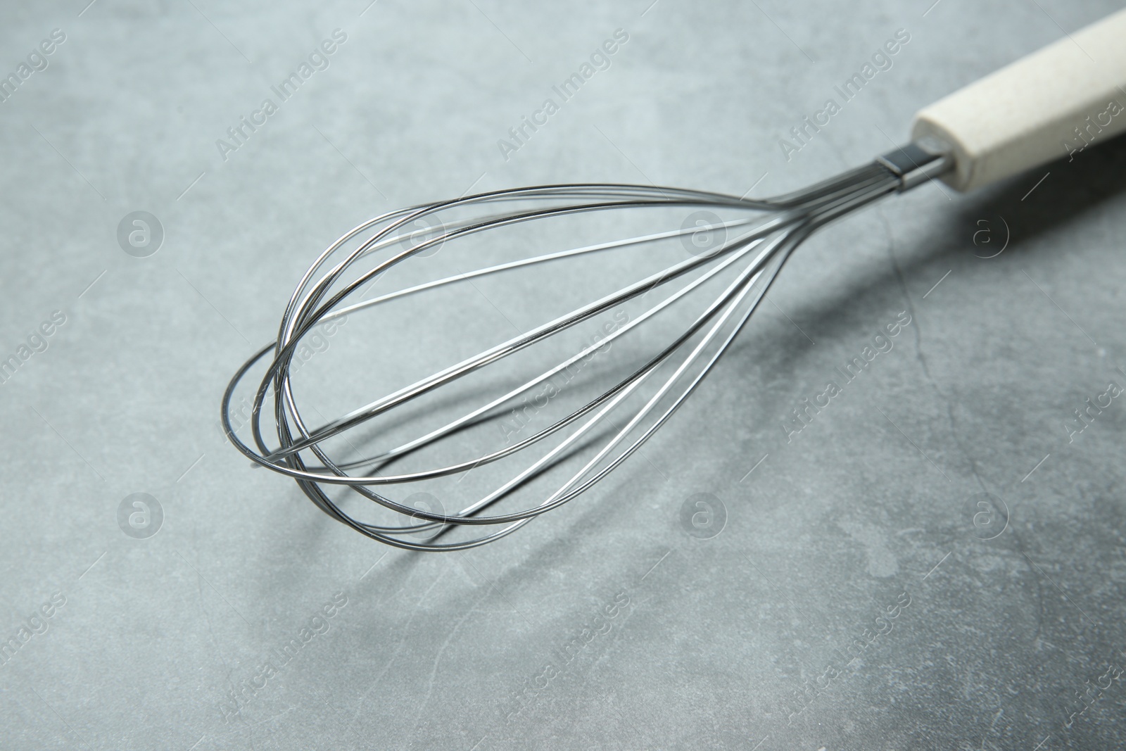 Photo of Metal whisk on gray table, closeup. Kitchen tool
