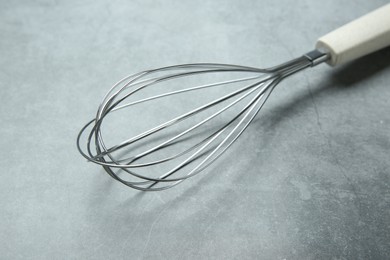 Photo of Metal whisk on gray table, closeup. Kitchen tool