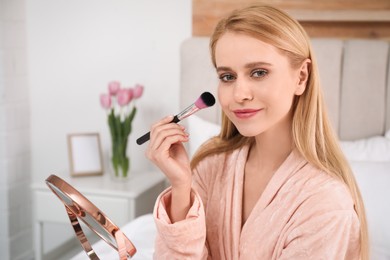 Beautiful woman with mirror applying makeup in bedroom