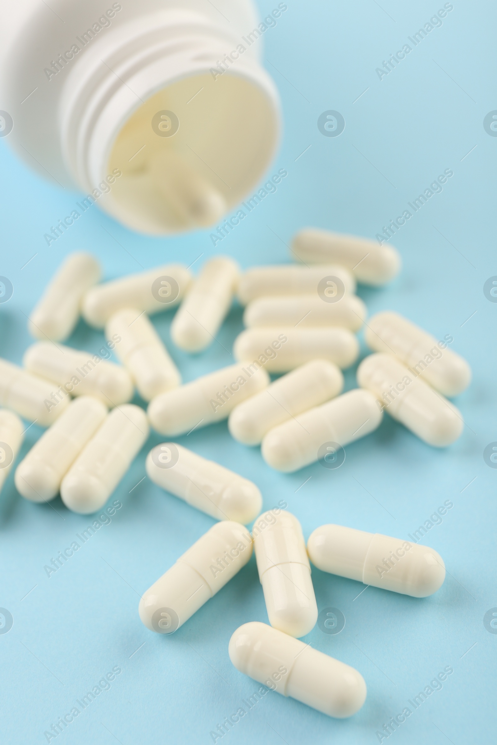 Photo of Bottle and vitamin capsules on light blue background, closeup