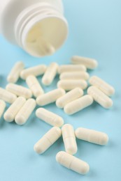 Photo of Bottle and vitamin capsules on light blue background, closeup