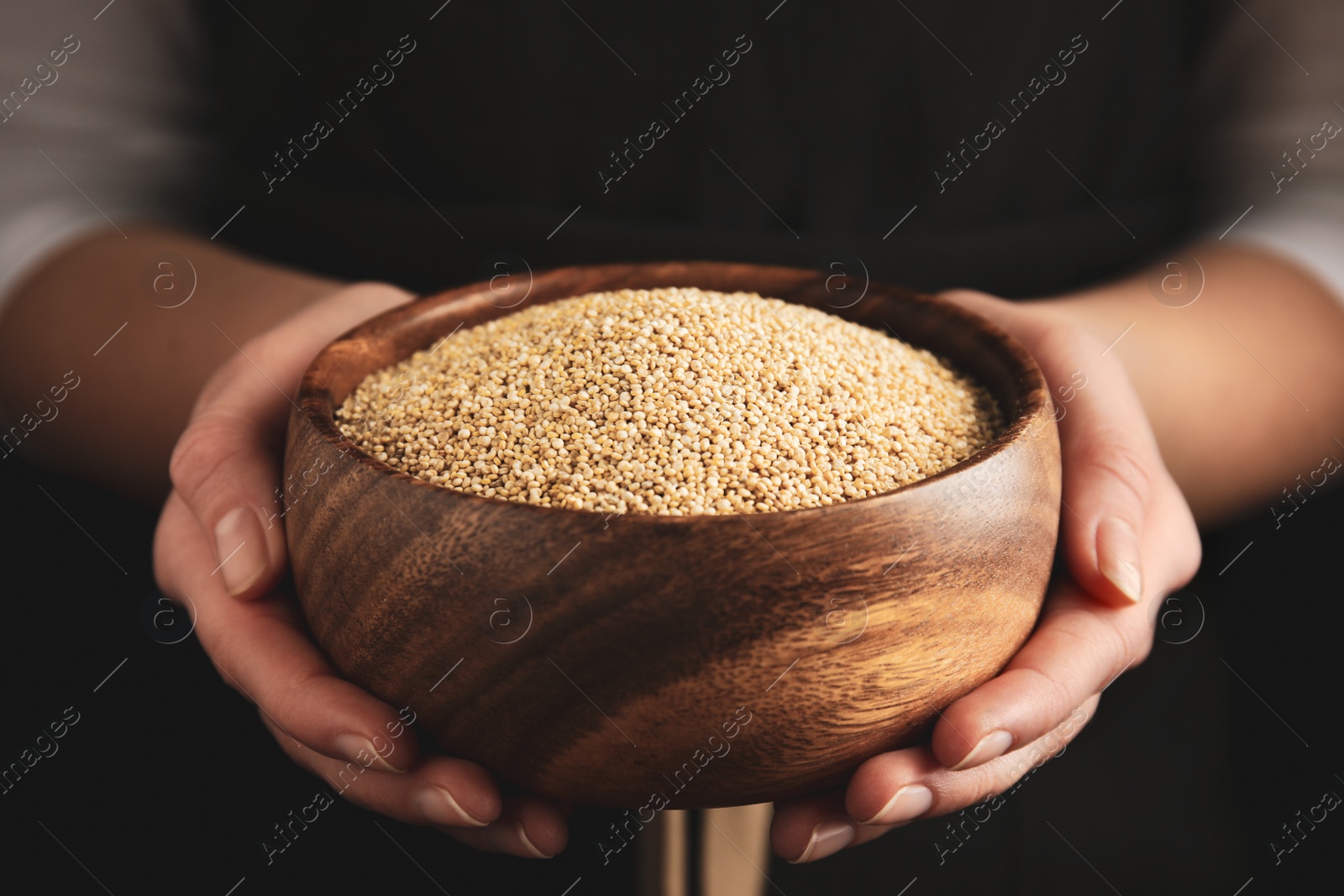 Photo of Woman holding wooden bowl with white quinoa on dark background, closeup