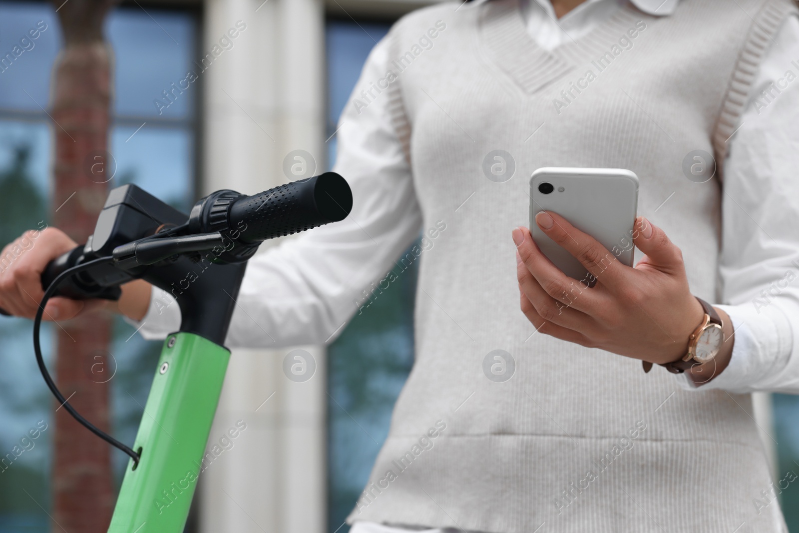 Photo of Businesswoman with modern kick scooter using smartphone on city street, closeup