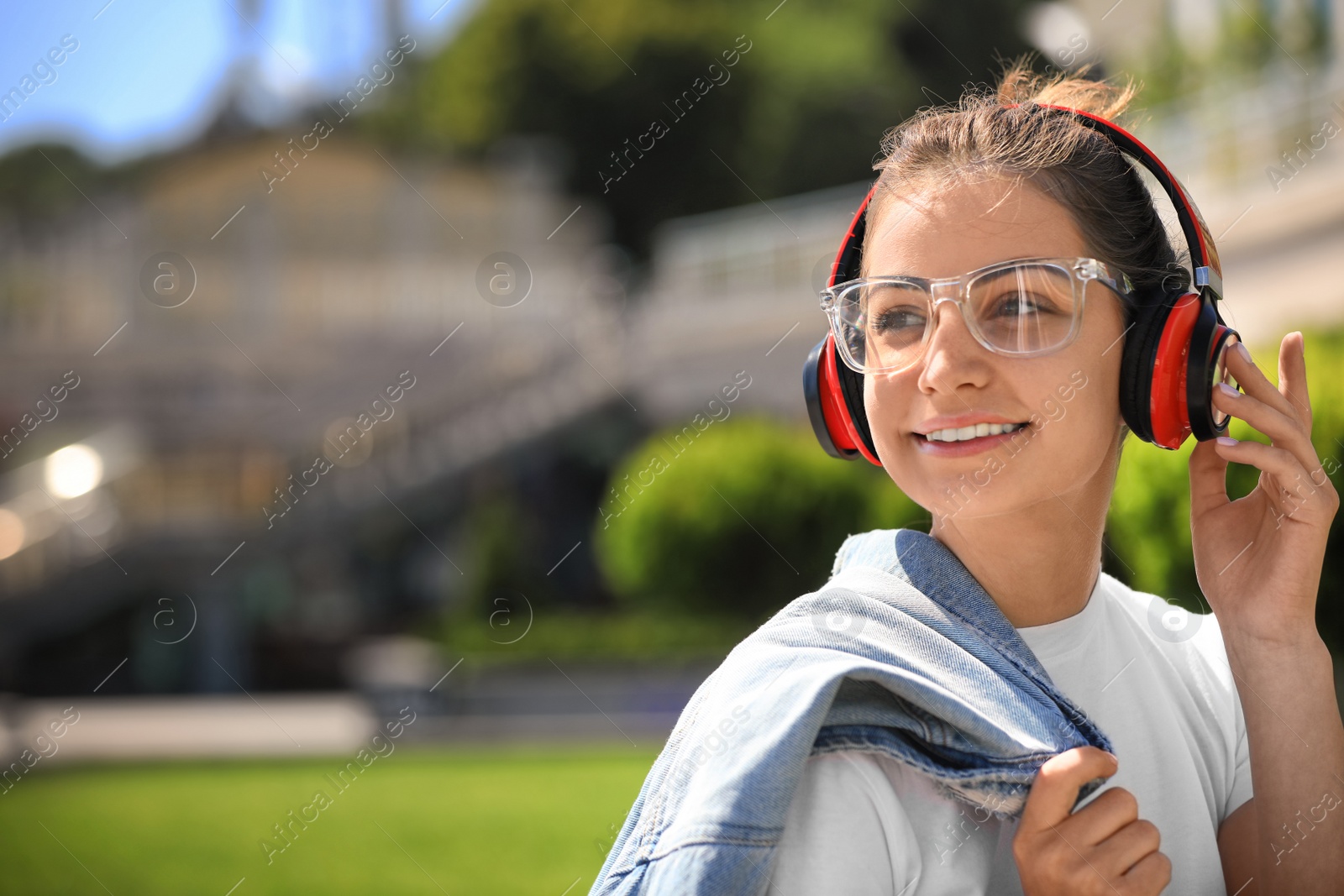Photo of Young woman with headphones listening to music on city street. Space for text