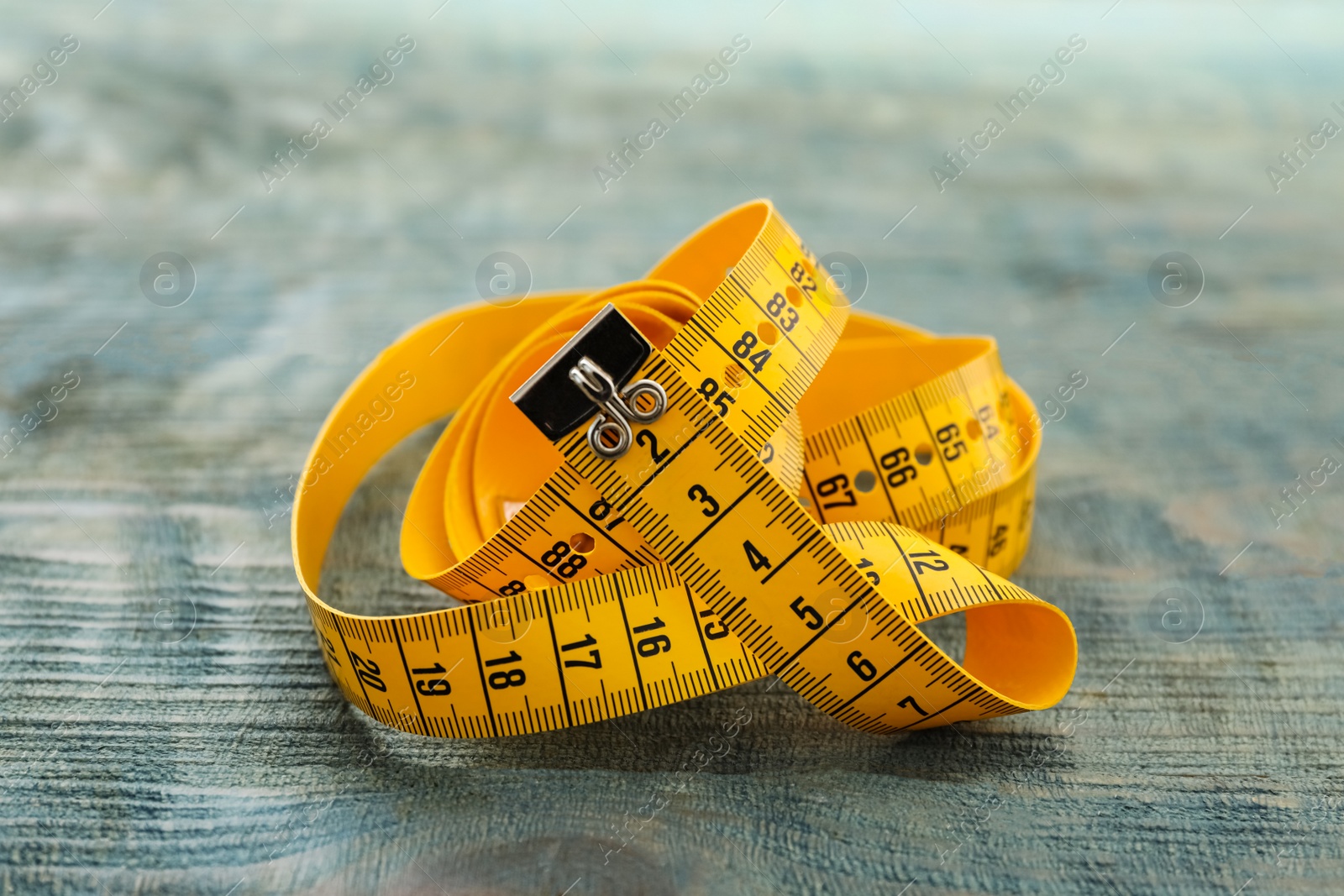 Photo of Yellow measuring tape on light blue wooden table, closeup