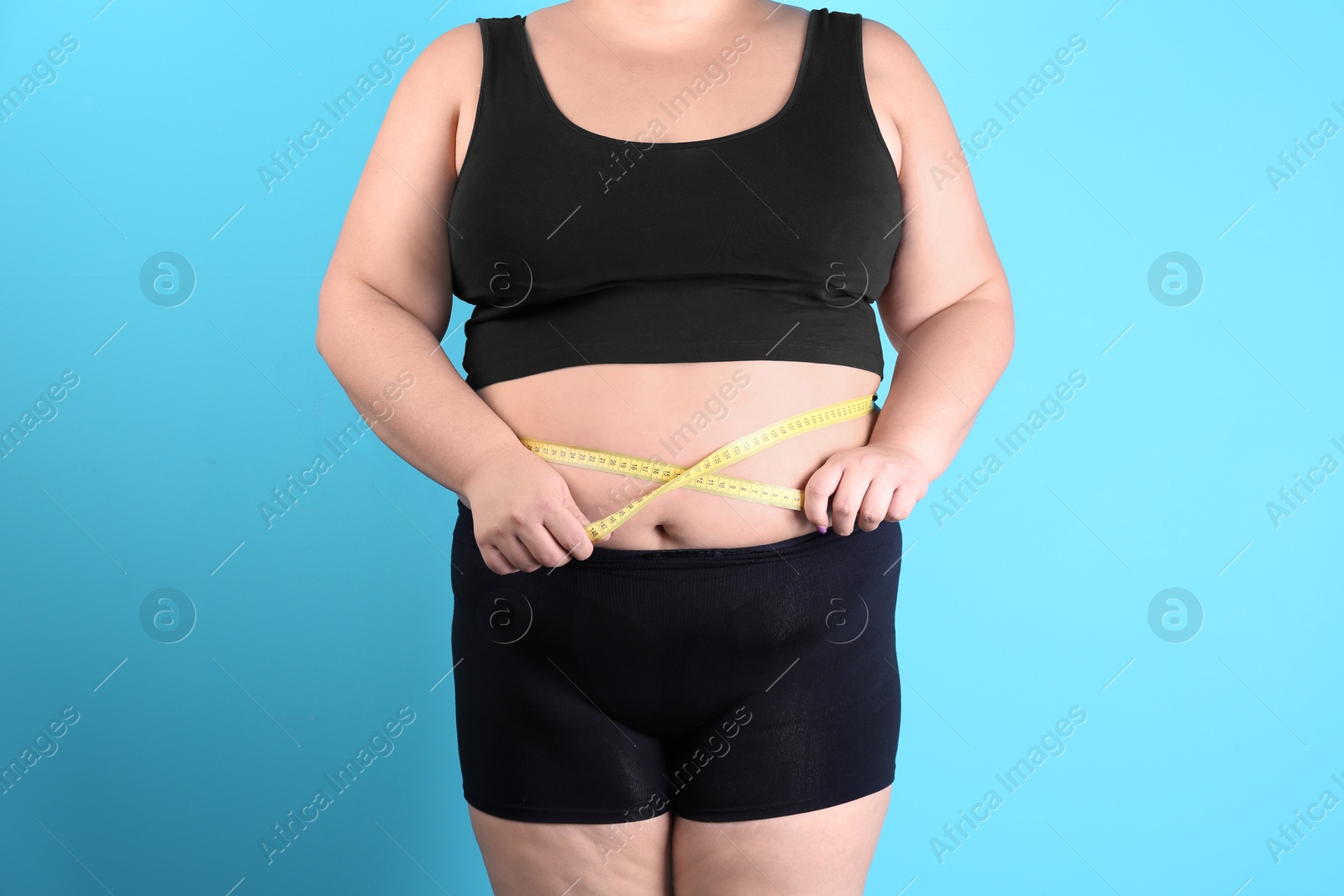 Photo of Overweight woman measuring waist before weight loss on color background