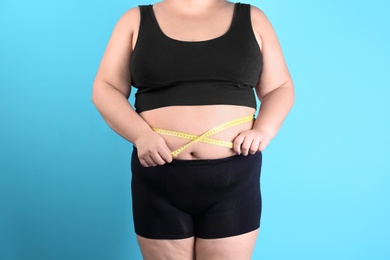 Overweight woman measuring waist before weight loss on color background