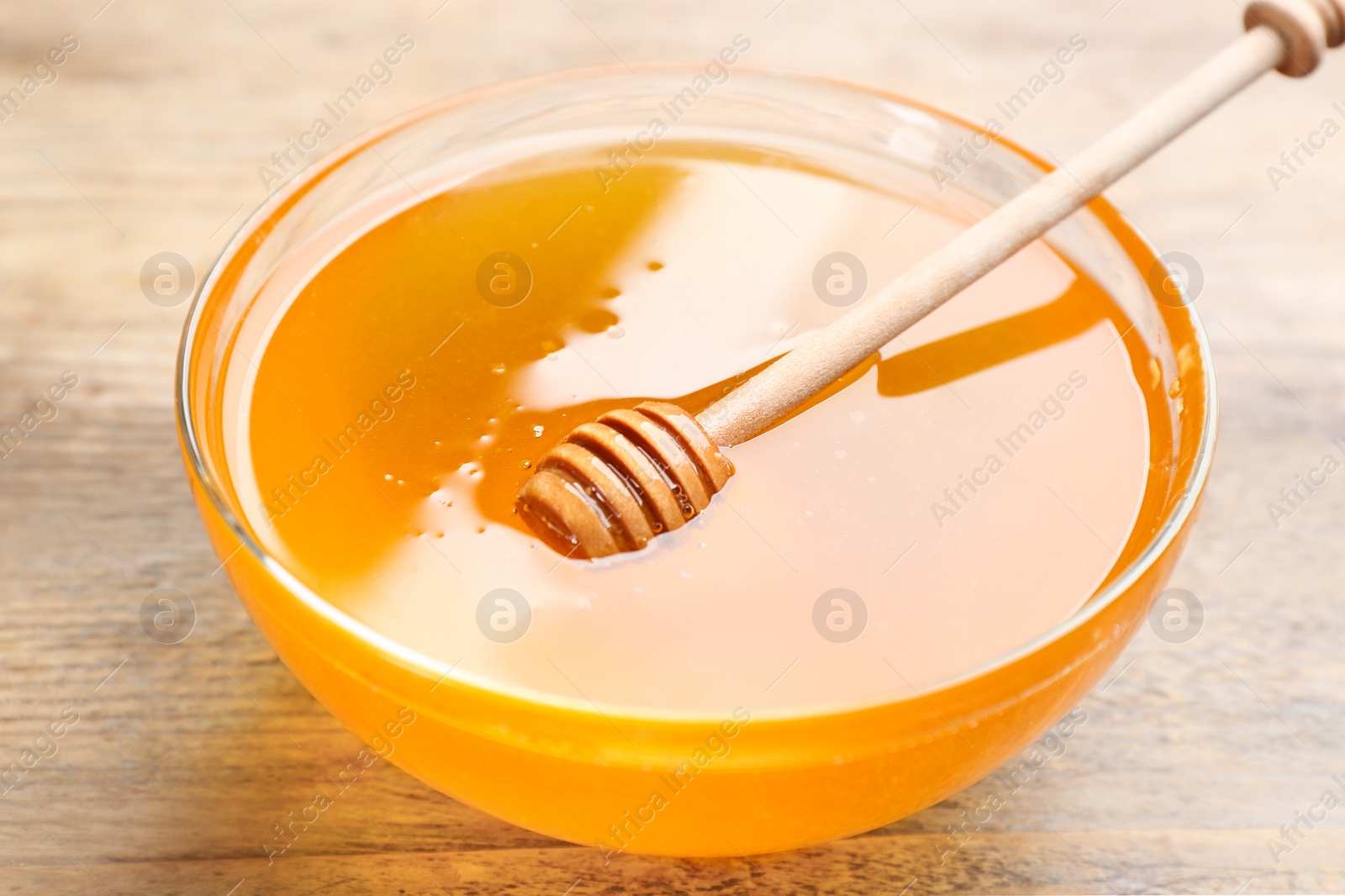 Photo of Tasty honey in glass bowl on wooden table, closeup