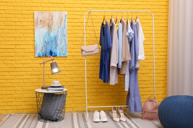 Photo of Rack with different stylish clothes and shoes near yellow brick wall in room