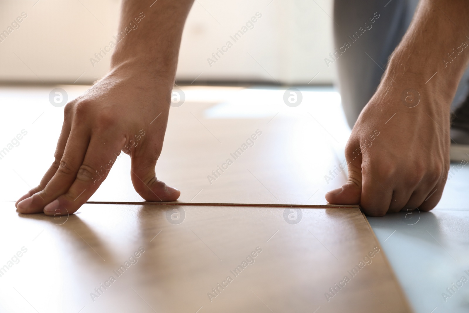 Photo of Worker installing laminated wooden floor indoors, closeup