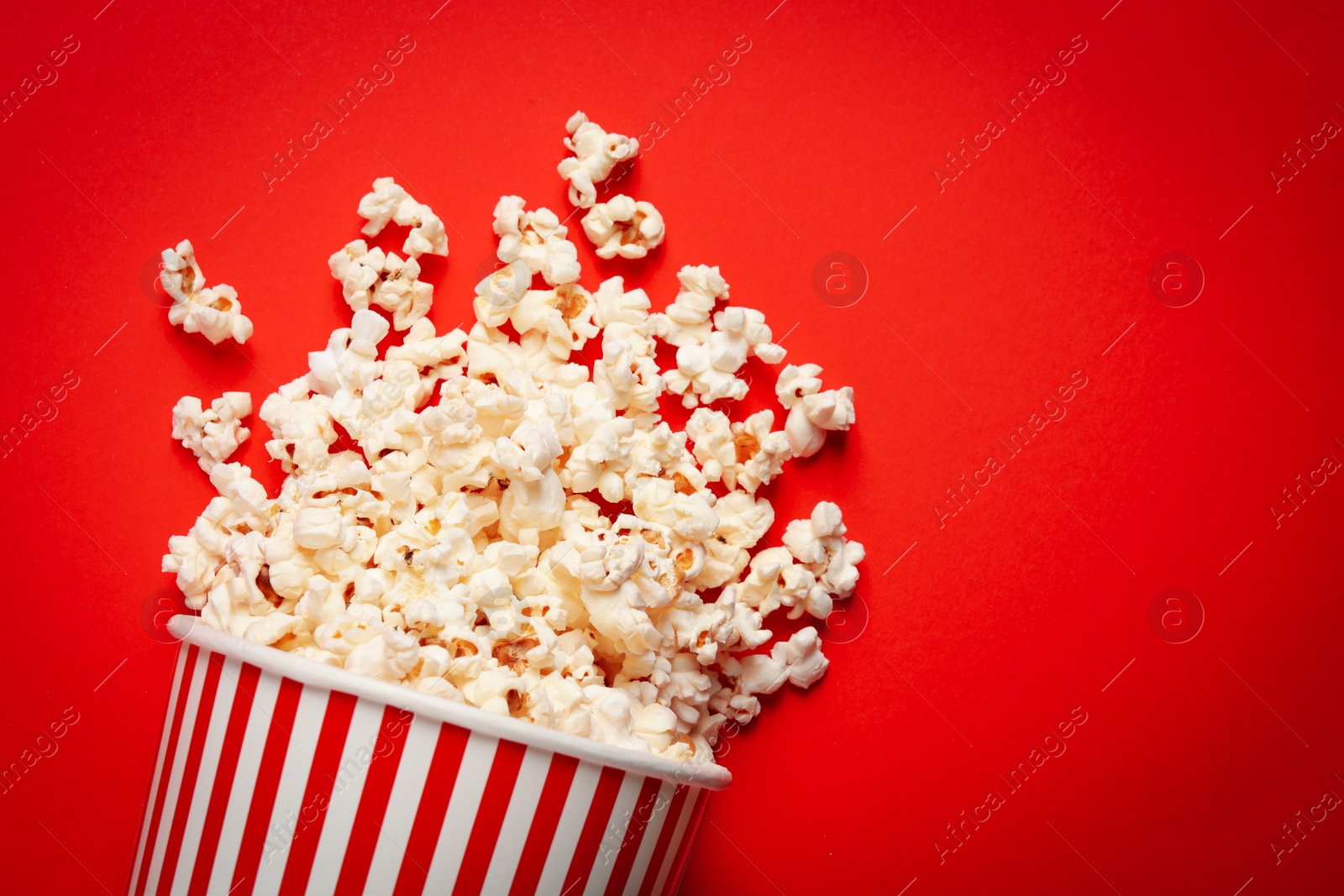 Photo of Overturned paper cup with delicious popcorn on red background, top view