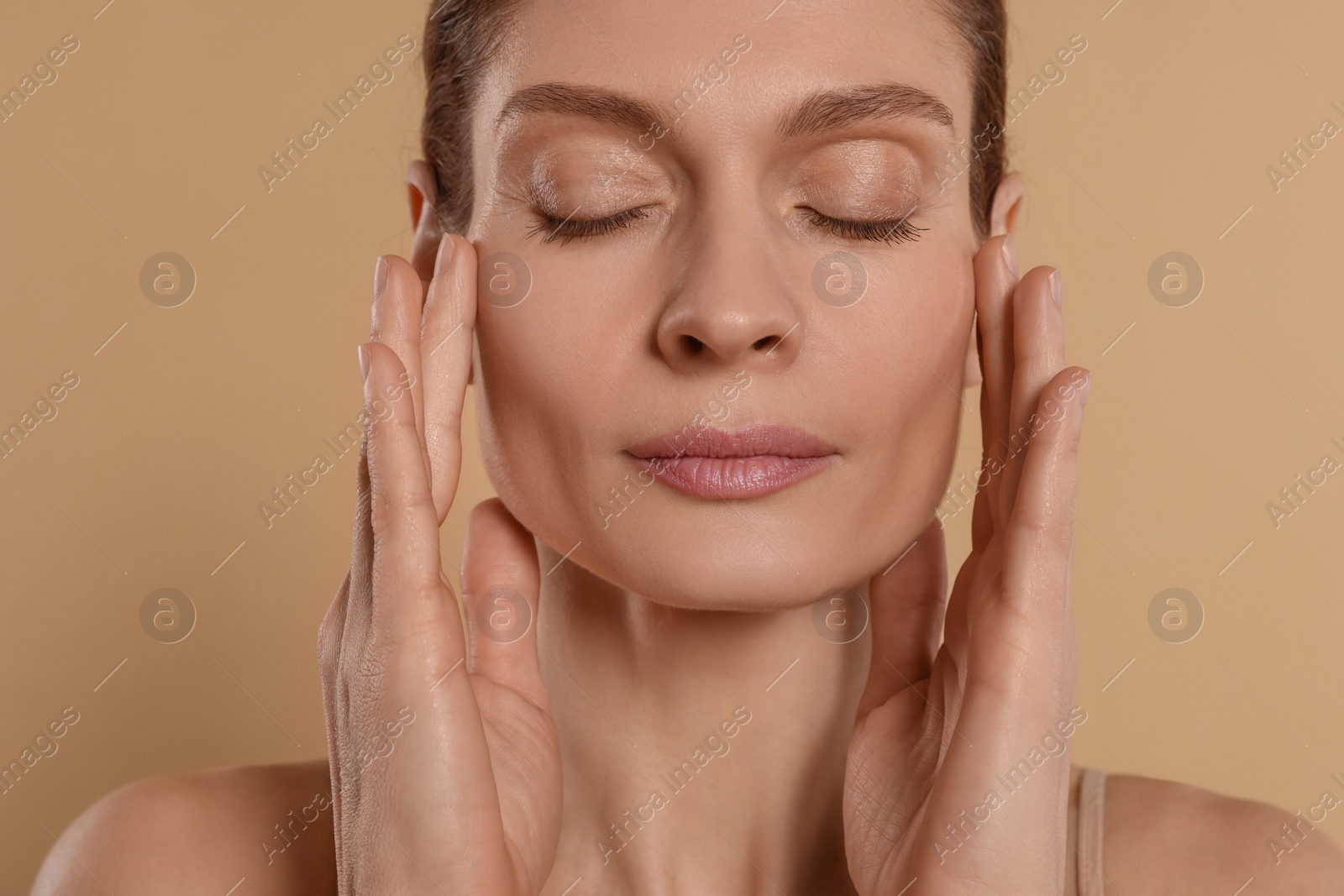 Photo of Woman massaging her face on beige background