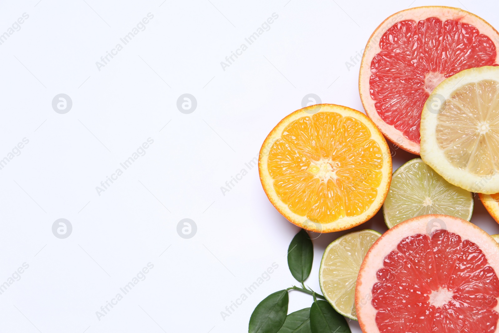 Photo of Different cut citrus fruits and leaves on white table, flat lay. Space for text