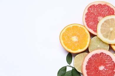 Different cut citrus fruits and leaves on white table, flat lay. Space for text