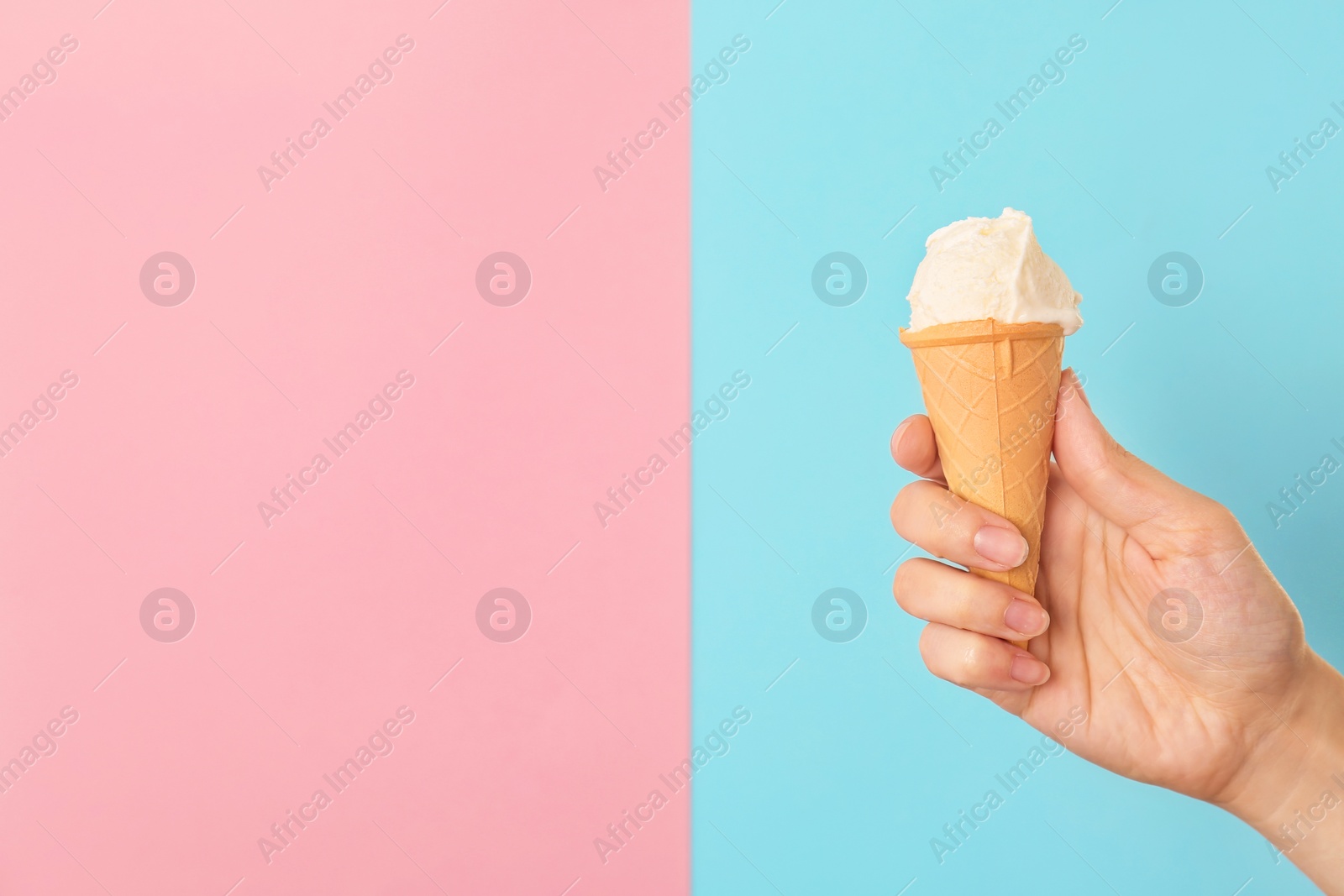 Photo of Woman holding waffle cone with tasty vanilla ice cream on color background