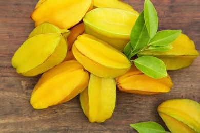 Delicious ripe carambolas with leaves on wooden table, flat lay