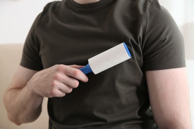 Man cleaning grey t-shirt with lint roller on light background, closeup