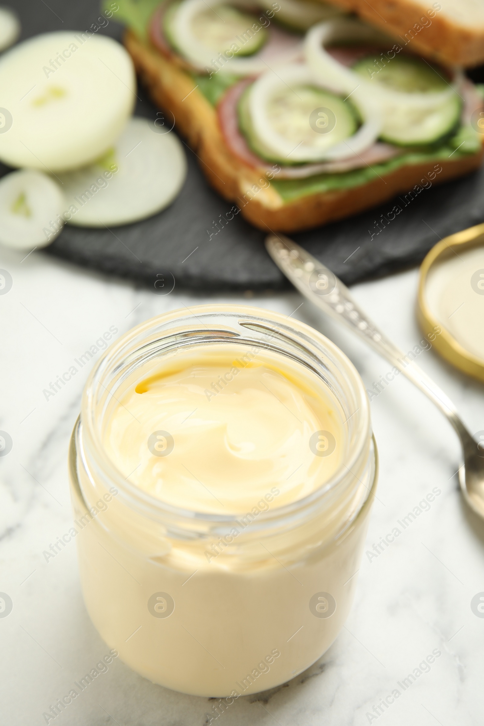 Photo of Jar of delicious mayonnaise near fresh sandwich on white marble table