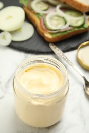 Jar of delicious mayonnaise near fresh sandwich on white marble table