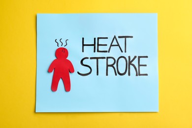 Photo of Note with words Heat Stroke and human cutout on yellow background, top view