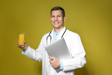 Nutritionist with glass of juice and laptop on yellow background
