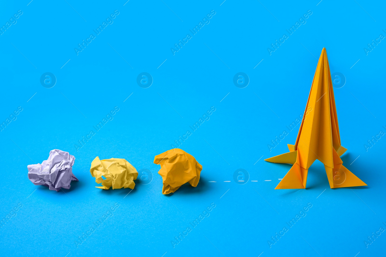 Photo of Handmade orange rocket and crumpled pieces of paper on light blue background