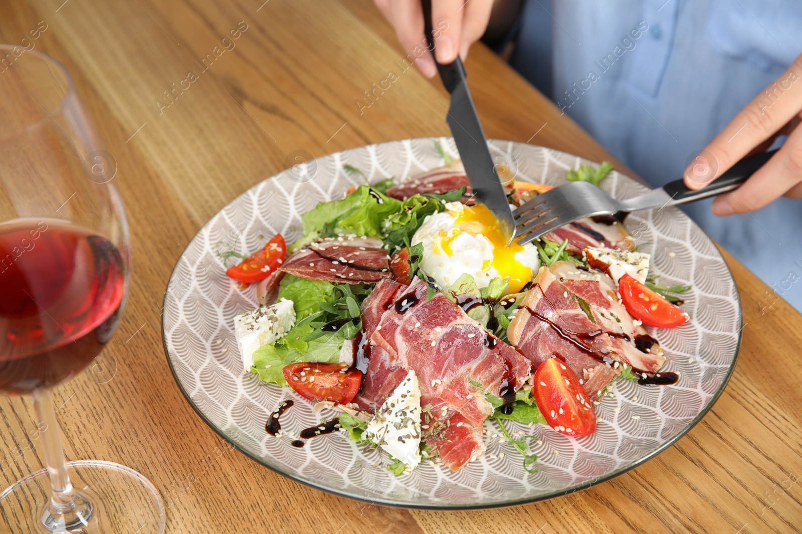 Photo of Woman eating delicious prosciutto salad with vegetables at wooden table, closeup