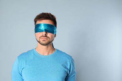 Young man with light blue blindfold on grey background, space for text