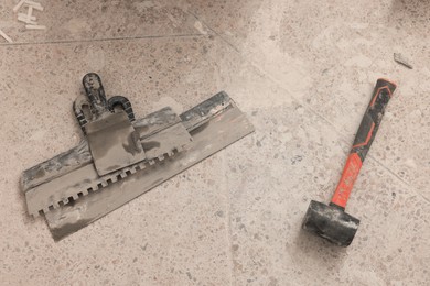 Photo of Metal spatulas and hammer on floor, above view. Tiles installation process