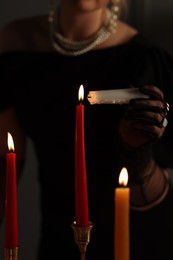 Woman with elegant jewelry lightning up candle indoors, closeup