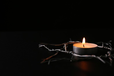 Photo of Burning candle and star of David made with barbed wire on black background, space for text. Holocaust memory day
