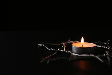 Burning candle and star of David made with barbed wire on black background, space for text. Holocaust memory day