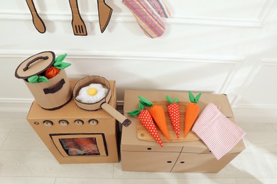 Photo of Toy cardboard kitchen with stove and utensils at home, above view