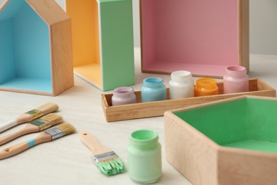 Photo of Jars of paints, brushes and house shaped shelves on white table. Interior elements